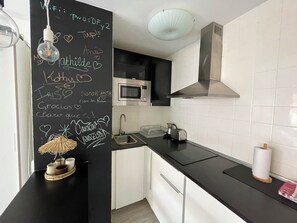 A modern kitchen with a blackboard, white cabinets, a microwave, and a sink.