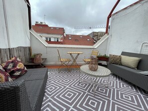 A rooftop terrace with a patterned floor, a sofa, a table, and chairs.