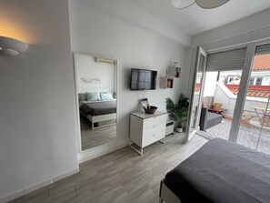 A bedroom with a bed, a dresser, a television, a potted plant, and a balcony with outdoor furniture.