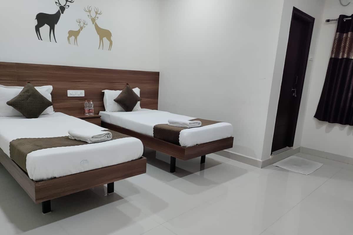 Une chambre d’hôtel avec deux lits simples, une tête de lit en bois, un mur décoré d’un motif représentant un cerf et une porte avec un rideau.