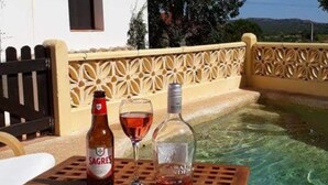 A table with a bottle of Sagres beer, a wine glass, and a bottle of liquor, set on a patio with a pool and a white building in the background. - Cosy country cottage with  plunge pool & bbq set in the peaceful countryside,


 (Sb de messines Silves)