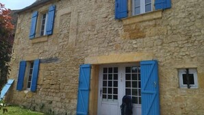 Ein Steinhaus mit blauen Fensterläden, einer weißen Tür und einem kleinen Fenster.