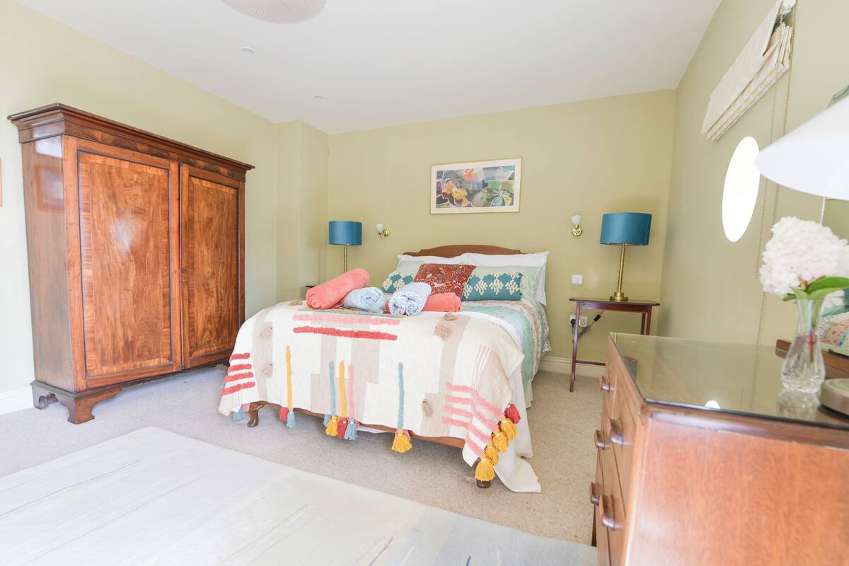 A bedroom with a bed, a wooden wardrobe, a bedside table with a lamp, and a mirror.