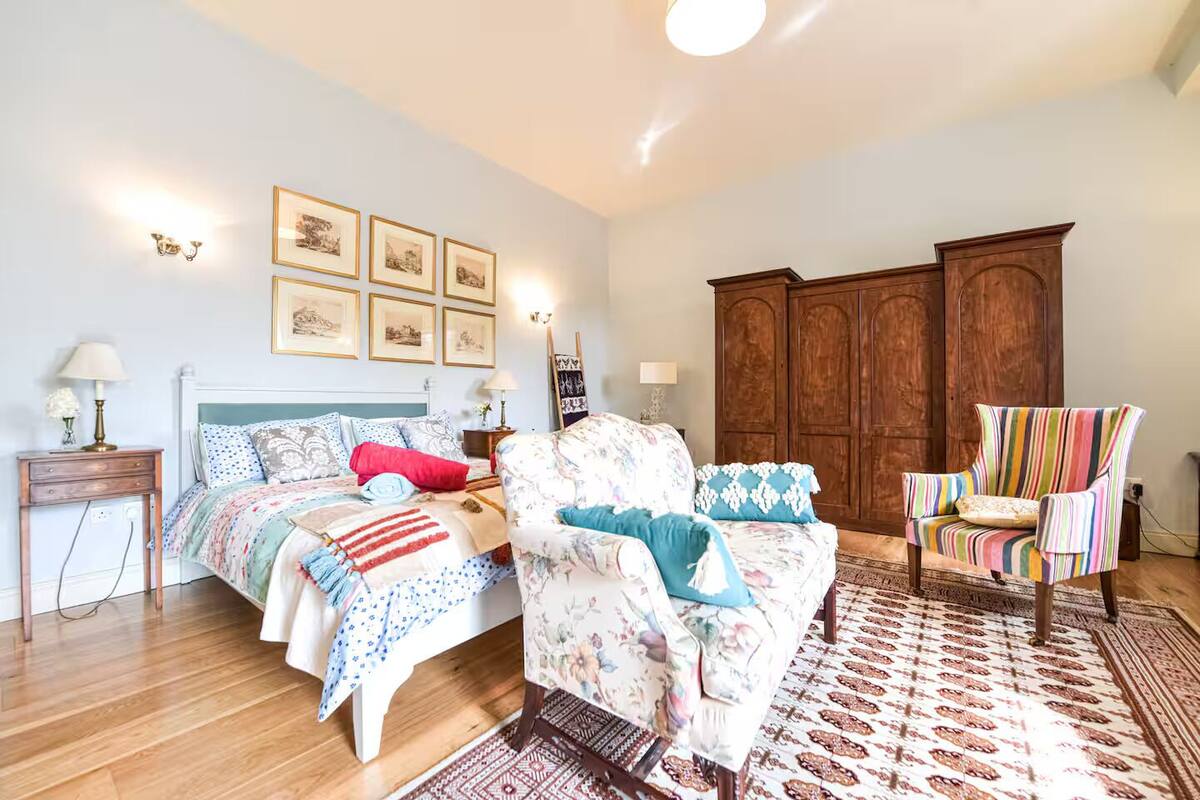 A bedroom with a bed, a chair, a wooden wardrobe, and wall-mounted picture frames.