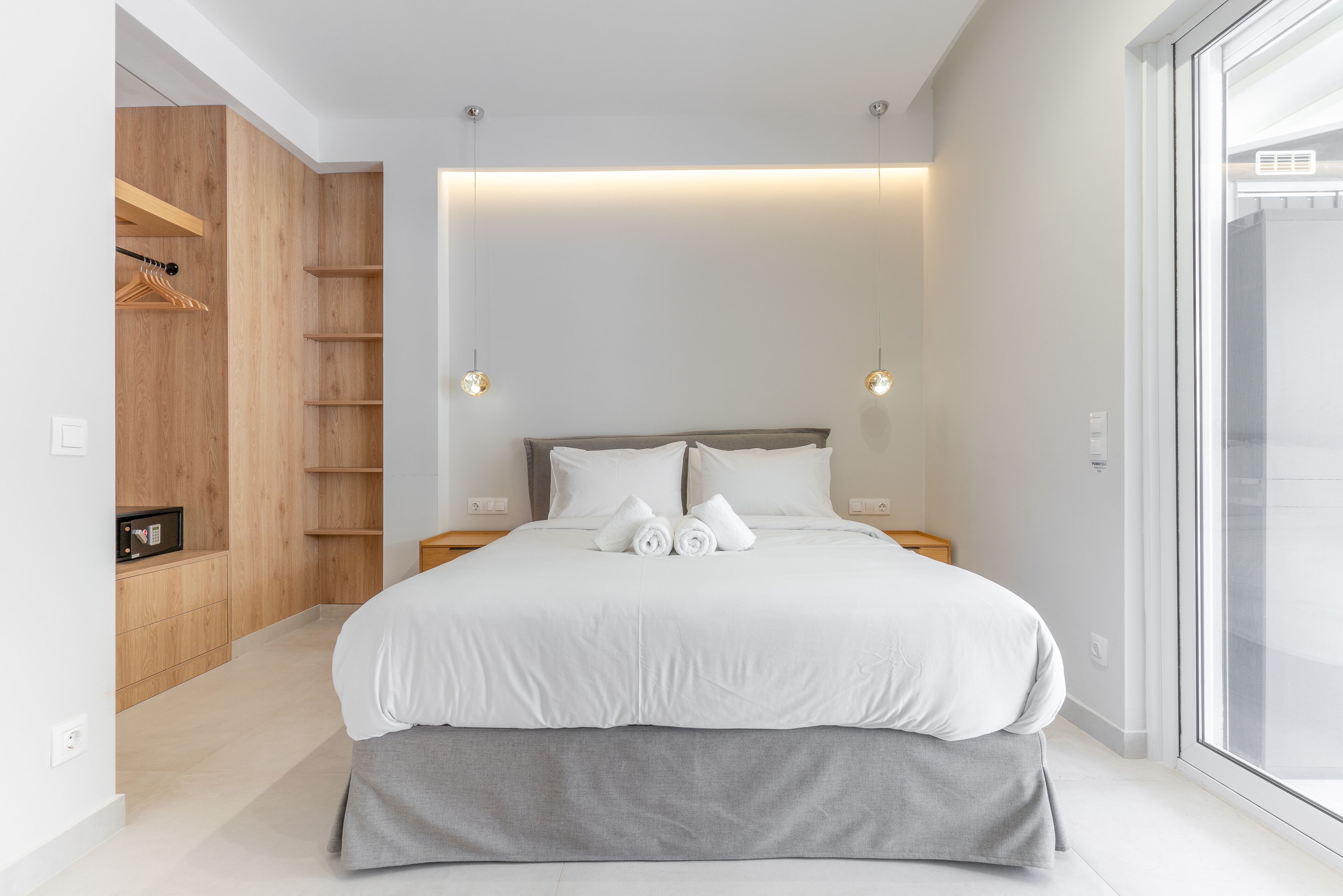 A modern bedroom with a large bed, wooden wardrobe, and a view through a glass door.
