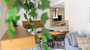 Een moderne woonkamer met een eethoek, een keuken op de achtergrond en een plantje op de voorgrond.