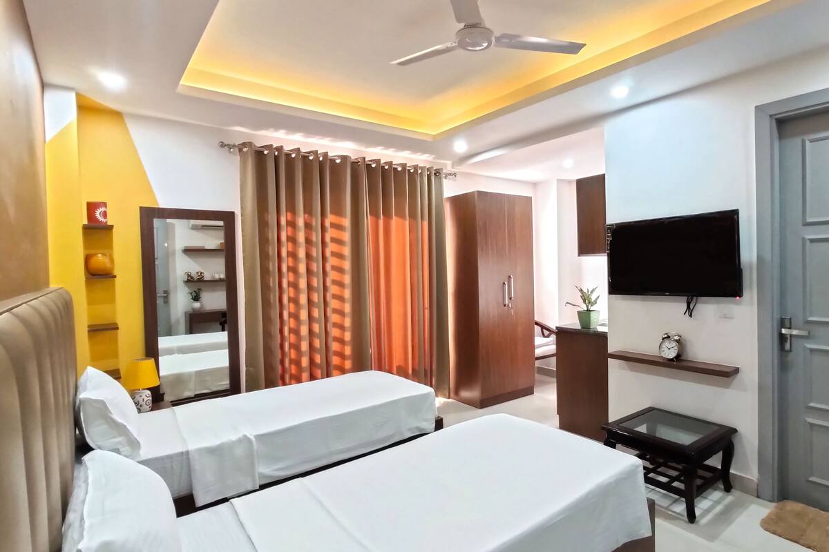 A hotel room with two beds, a ceiling fan, a TV mounted on the wall, a small table, and a wardrobe.