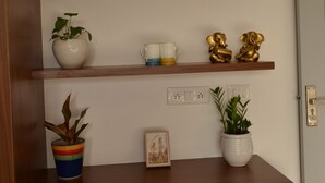 A wooden desk with shelves holding decorative items, a potted plant, and a framed picture. - Covie Gurgaon 108 (Gurugram)