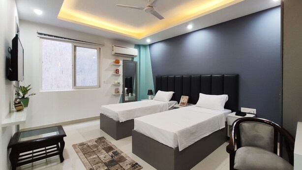 A modern hotel room with two beds, a ceiling fan, a flat-screen TV, and a window with blinds. - Covie Gurgaon 108 (Gurugram)