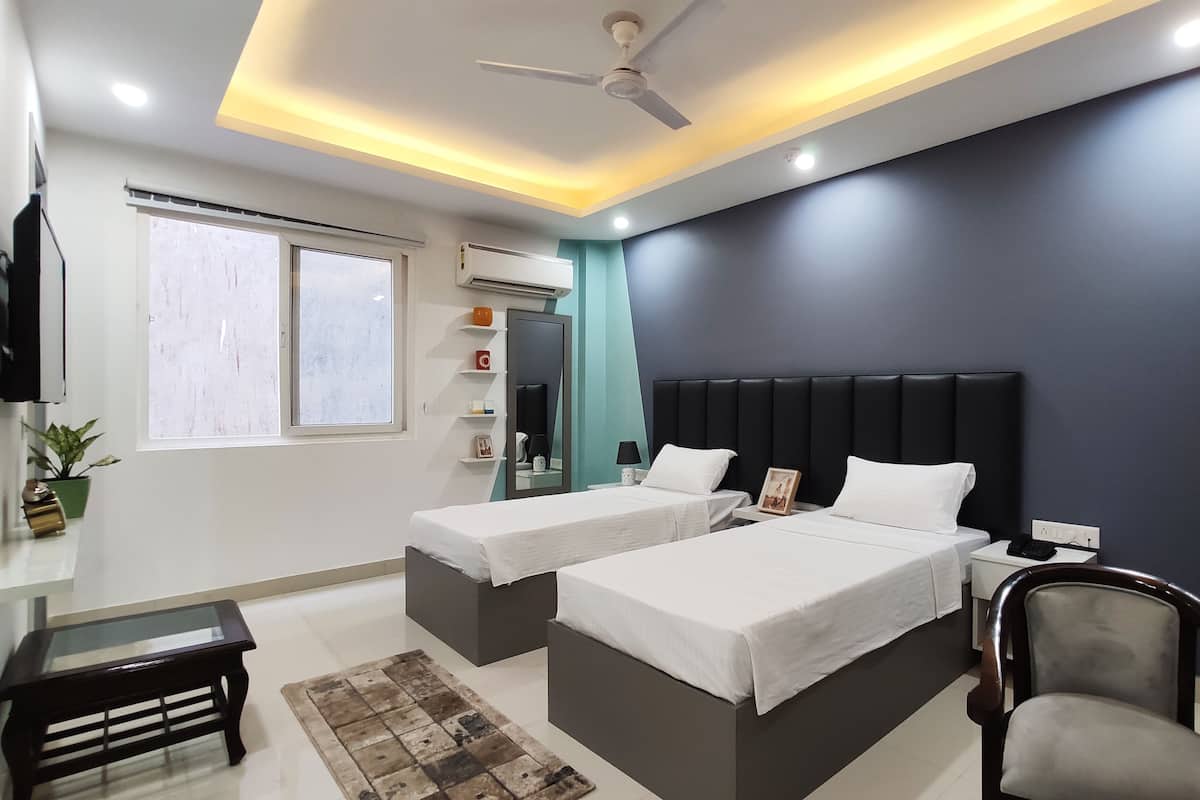 A modern hotel room with two beds, a ceiling fan, a flat-screen TV, and a window with blinds.