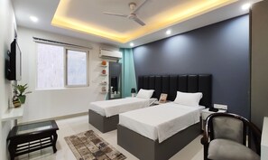 A modern hotel room with two beds, a ceiling fan, a flat-screen TV, and a window with blinds. - Covie Gurgaon 108 (Gurugram)