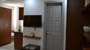 A modern living room with a flat-screen TV mounted on the wall, a wooden cabinet, a small table, and a door. - Covie Gurgaon 108 (Gurugram)