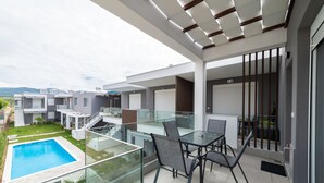 Un patio moderno al aire libre con una mesa y sillas de vidrio, una piscina y vistas a casas vecinas.