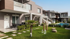Un moderno edificio residencial de varios pisos con piscina, mobiliario exterior y un jardín bien cuidado.