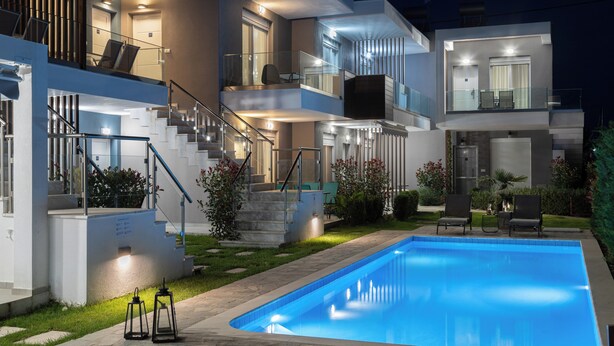 Una casa moderna de dos pisos con piscina, mobiliario exterior y una escalera bien iluminada.