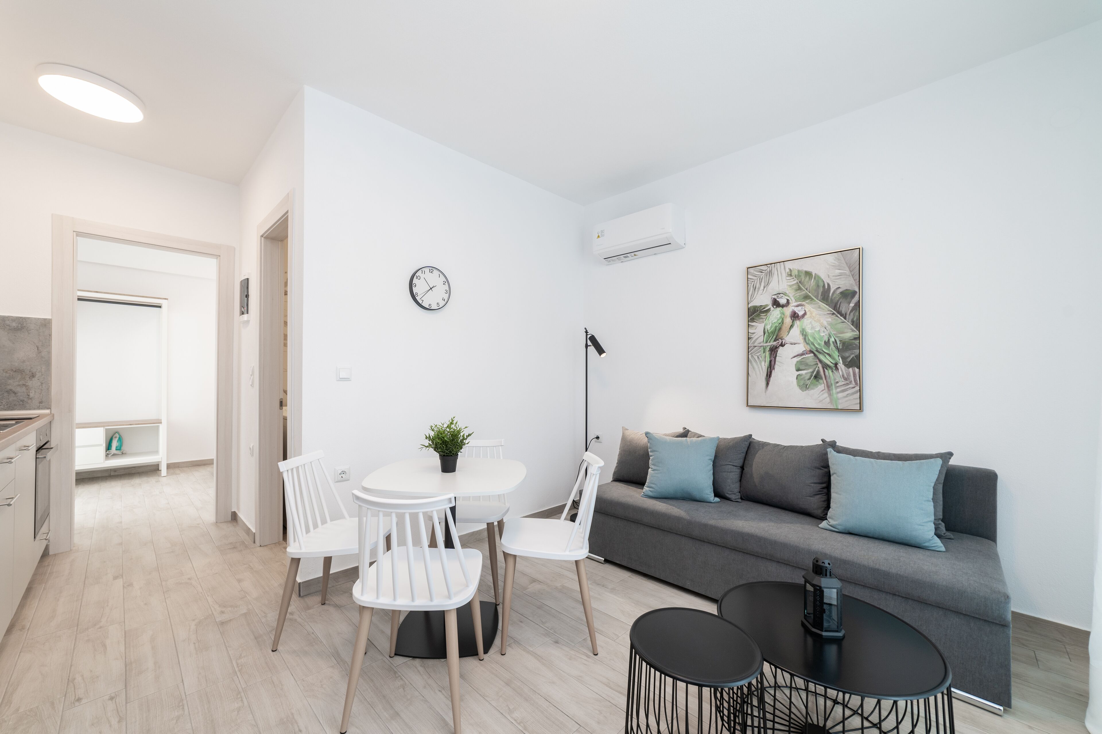 A modern living room with a grey sofa, white chairs, a round table, and a painting on the wall.