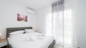 Una habitación de hotel moderna con una cama grande, una mesita de noche, aire acondicionado instalado en la pared, una ventana con cortinas translúcidas y un cuadro con una imagen de un parque.