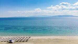 Una playa con hileras de sombrillas y sillas, cielo despejado y mar tranquilo.