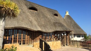 A thatched-roof building with large windows and a stone staircase leading to the entrance.