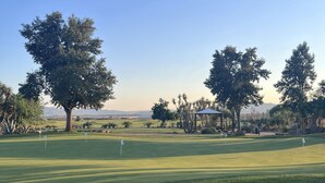 A golf course with well-maintained grass, several trees, and a pavilion.