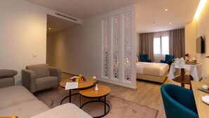 Et hotelværelse med sofa, lænestol, spisebord og seng med et sengebord.