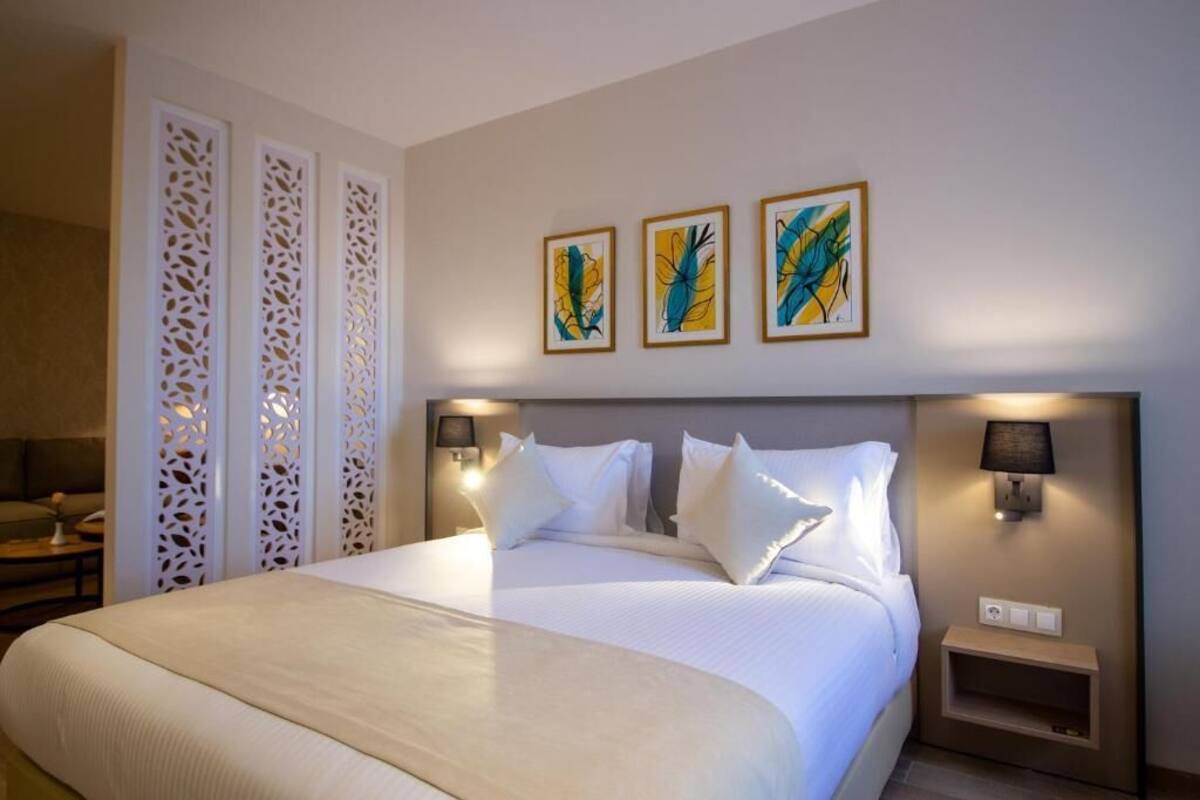 A hotel room with a large bed, white bedding, decorative wall panels, and three framed artworks.