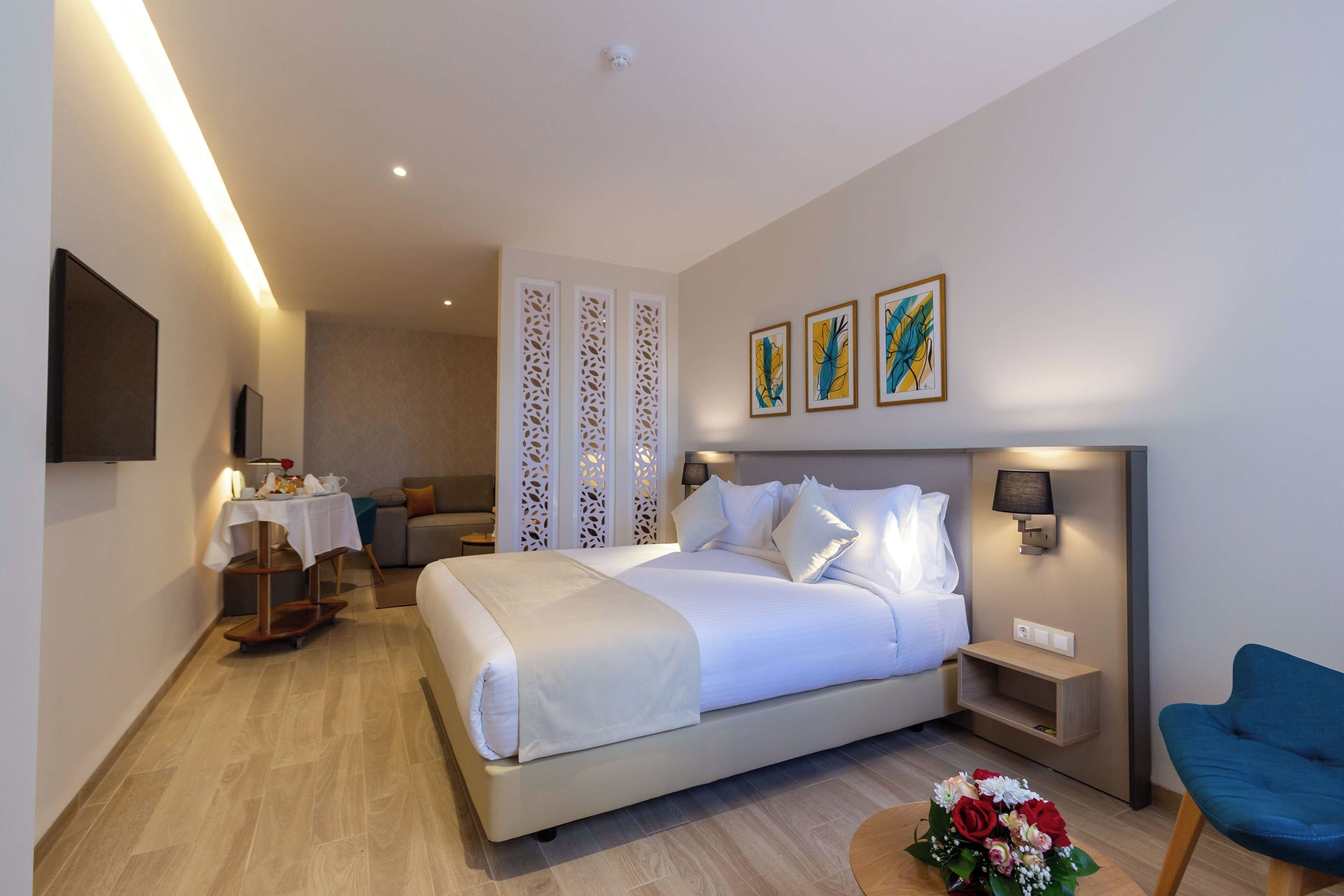 Una habitación de hotel con cama, mesita de noche, lámpara, una obra de arte y una silla.
