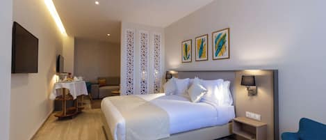 A hotel room with a bed, bedside table, lamp, artwork, and a chair.