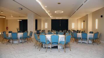 Une salle de conférence dotée de tables rondes et de chaises bleues, équipée de luminaires au plafond et recouverte d’un tapis.