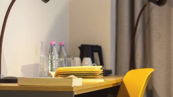 A desk with a lamp, a chair, a stack of papers, and two bottles on it.