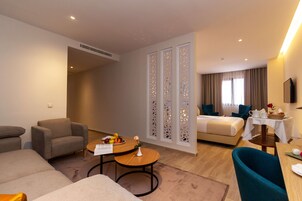 A hotel room with a sofa, armchair, dining table, and a bed.