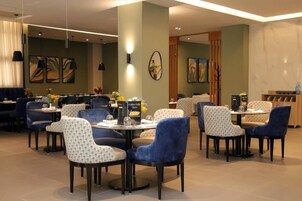 Un comedor moderno con mesas redondas y sillas azules, con obras de arte en las paredes y un atril para el menú.