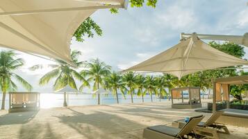 Relax on the beach with lounge chairs and umbrellas, surrounded by palm trees and a clear ocean view.
