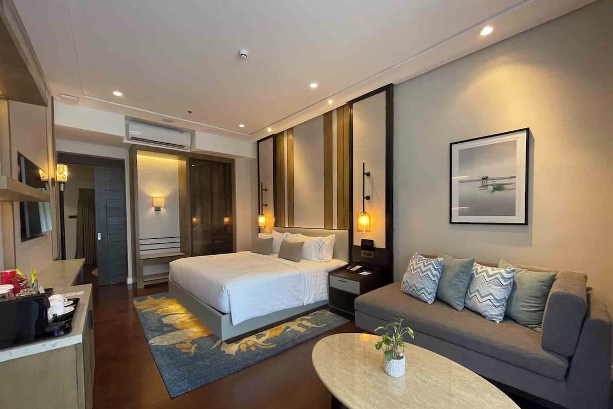 A modern hotel room with a bed, a sofa, a coffee table, and a large mirror.