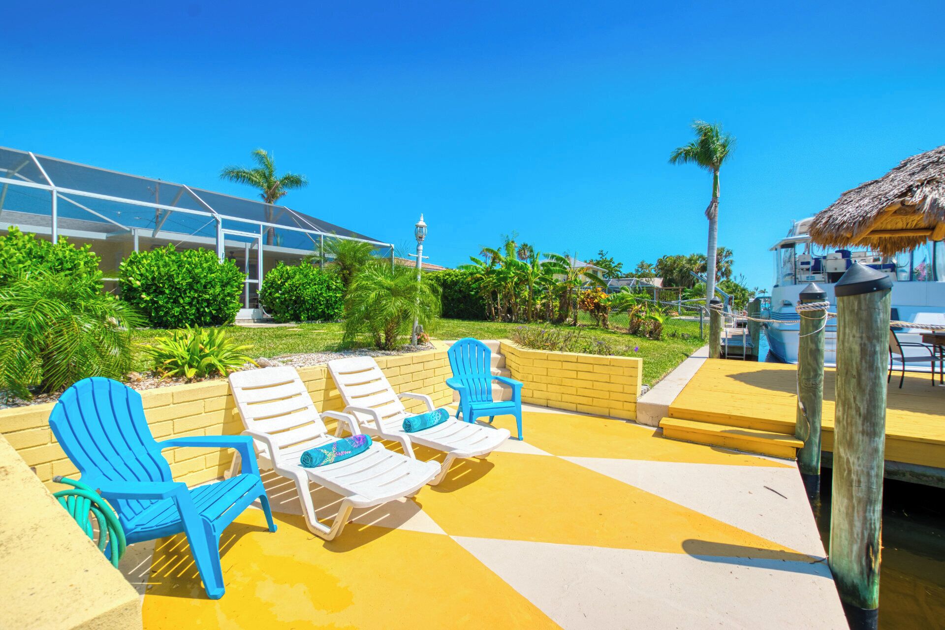 Un espace aménagé au bord de la piscine, avec des chaises longues, une structure à toit de chaume et un bateau amarré à proximité.