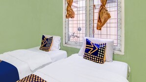 A room with two beds, each with a white mattress and blue and yellow patterned pillows. There is a window with metal bars and curtains.