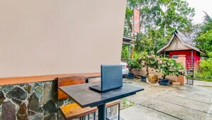 A stone wall, a table with a laptop, and a small red structure in a garden.
