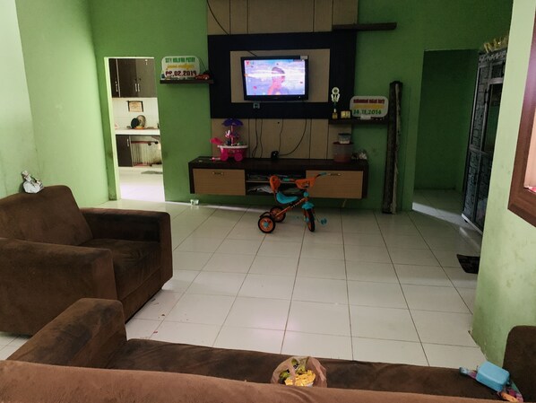 Un salón con paredes verdes, un televisor montado en la pared, un sofá marrón, una mesita con un juguete y un armario.