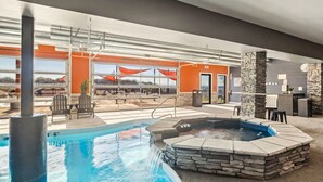 Une piscine intérieure avec un jacuzzi, des murs en pierre et un espace extérieur aménagé pour se détendre.
