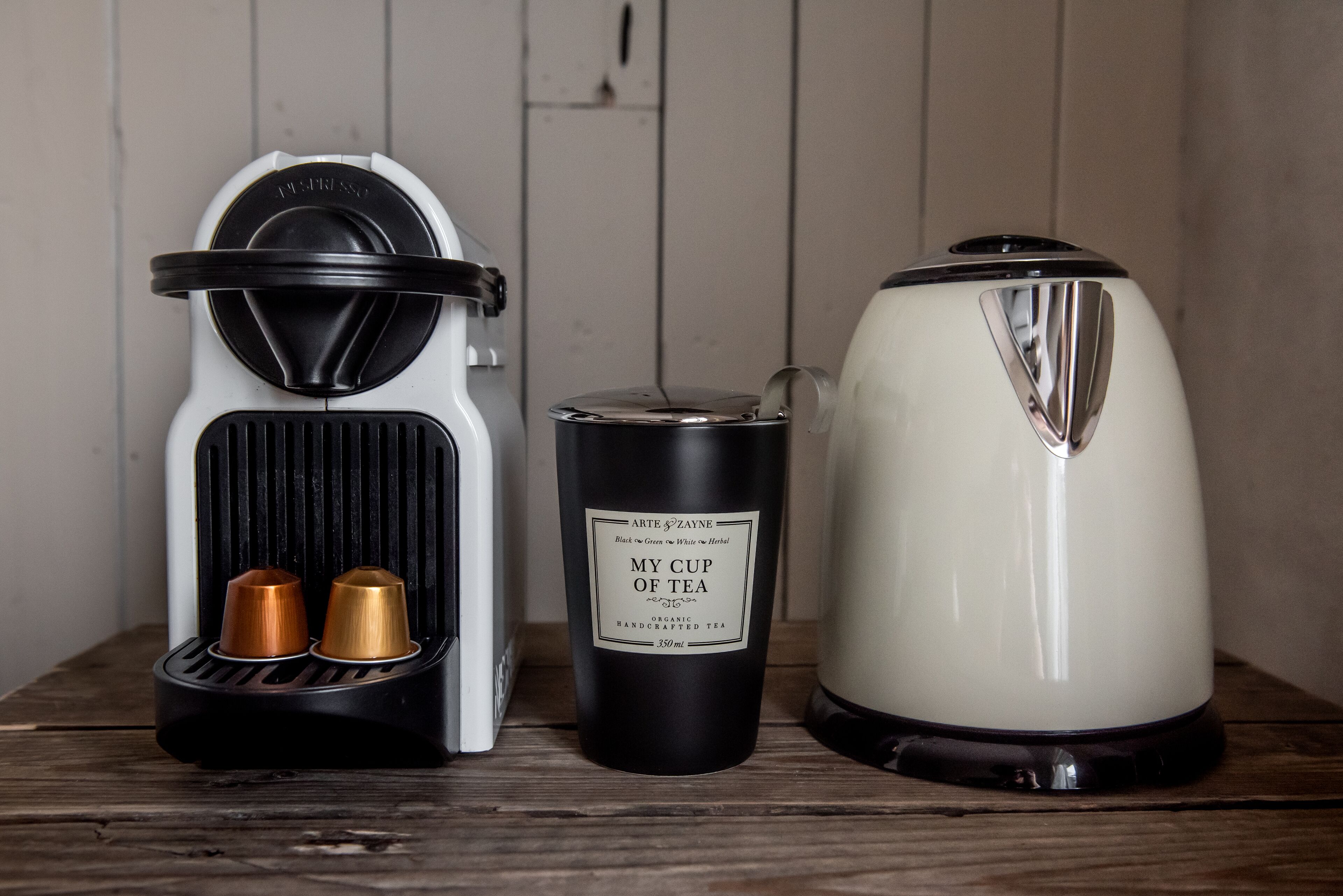 Eine Kaffeemaschine, ein schwarzer Thermosbehälter und ein weißer Wasserkocher auf einer Holzplatte.