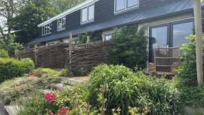 Een modern huis met een donkere gevel, een houten omheining en een tuin met diverse planten en bloemen.