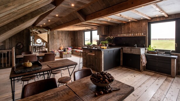 Een rustieke keuken met houten balken, een eethoek met een grote tafel en uitzicht op het landschap.