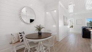 A dining area with a round wooden table, white chairs, a mirror with a white frame, and a potted plant.