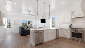 A spacious kitchen with white cabinetry, a central island, stainless steel appliances, pendant lighting, and a ceiling fan.
