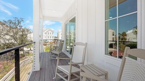 A covered porch with wooden flooring, white wicker chairs, and a view of neighboring houses.