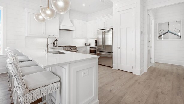 A modern kitchen with white cabinetry, stainless steel appliances, and a large island with bar stools.