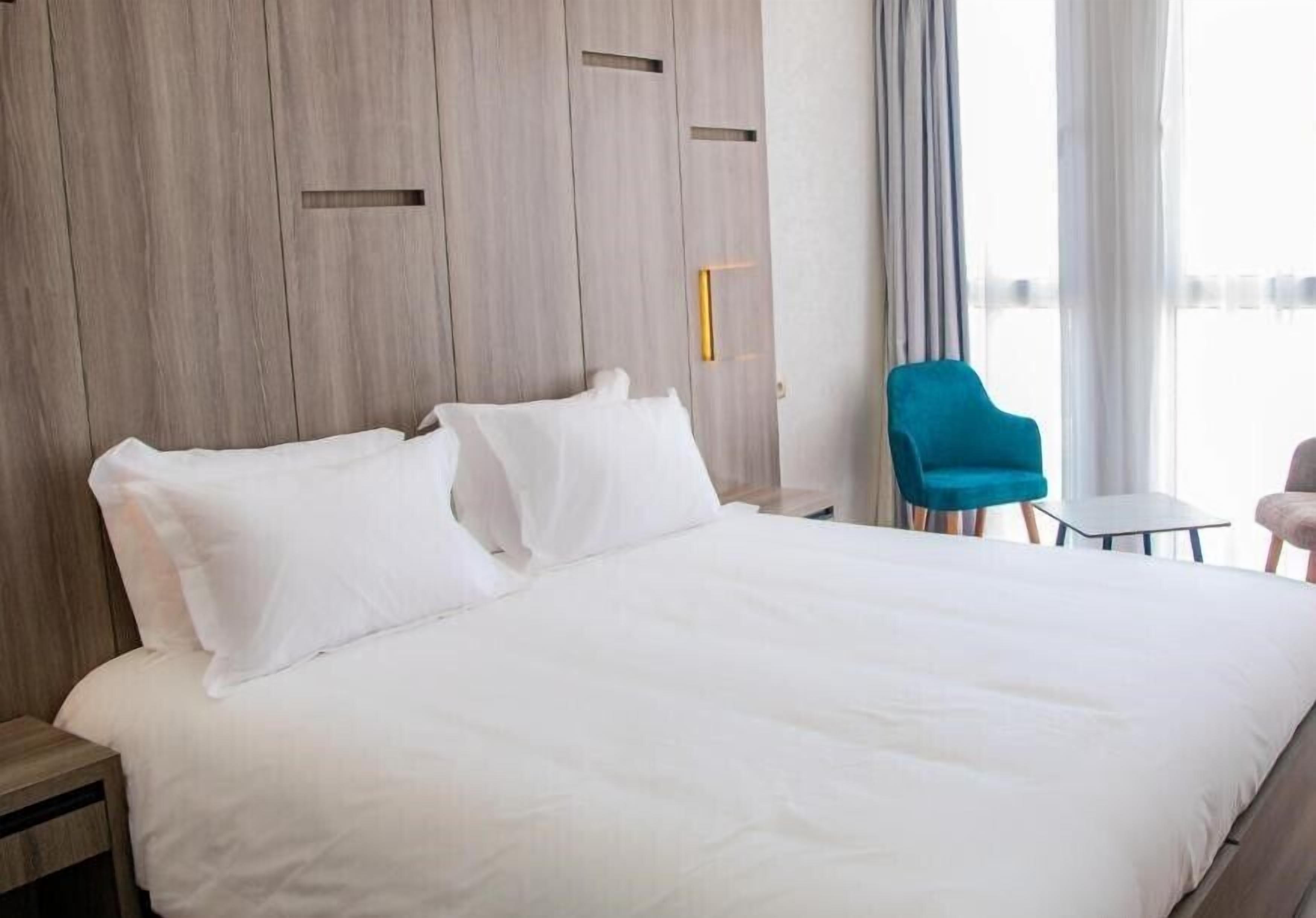 Une chambre d’hôtel avec un grand lit, une armoire en bois, une chaise bleue et une petite table.