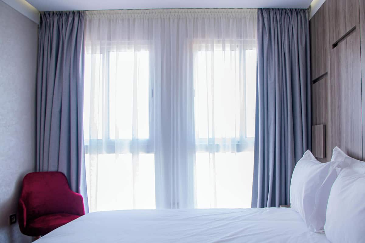 Ein Hotelzimmer mit einem Bett, einem roten Sessel und einem großen Fenster mit Vorhängen.