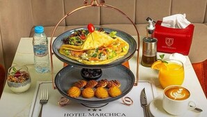 A breakfast setup with a two-tiered serving tray, a bottle of water, a glass of orange juice, a cup of coffee, and a napkin box. - Marchica Hotel (Nador)