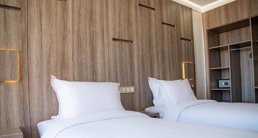Habitación de hotel con dos camas, paredes de paneles de madera, un armario y una mesita de noche.